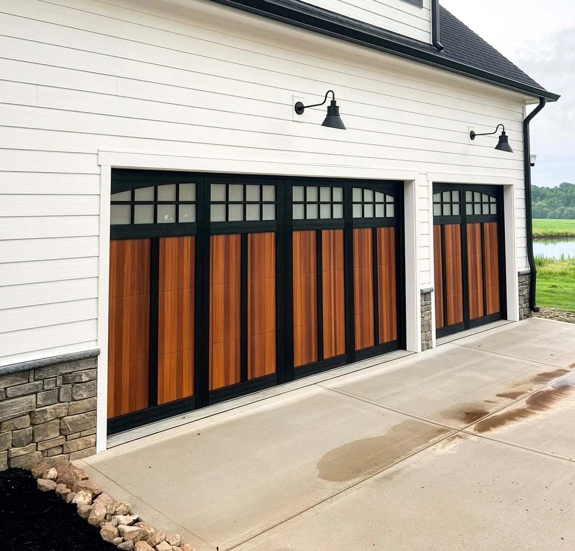 Two-tone garage doors with black frames, cedar-look panels, and arched divided-light windows