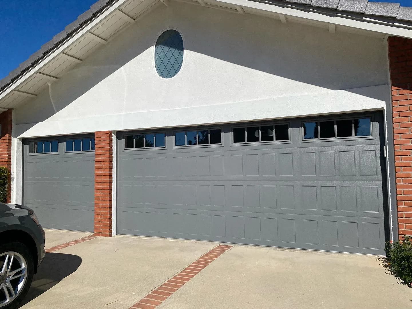 Gray long-panel steel garage doors on a stucco home with red brick columns