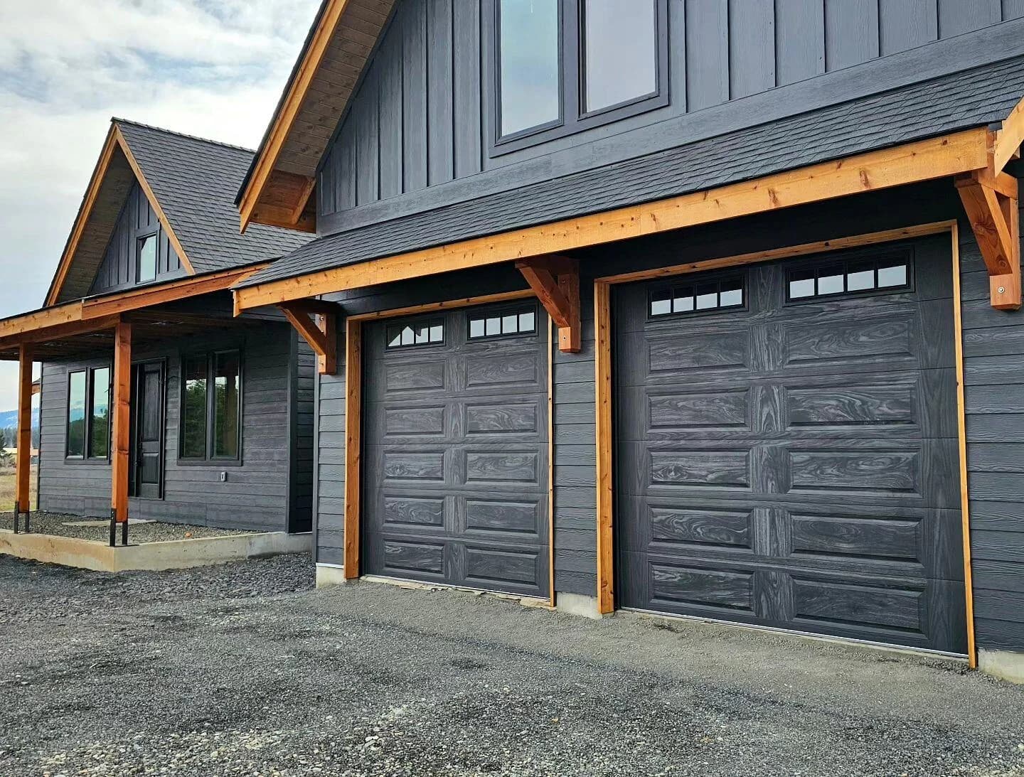 Dark grey raised-panel steel garage doors with a row of top windows on a modern farmhouse