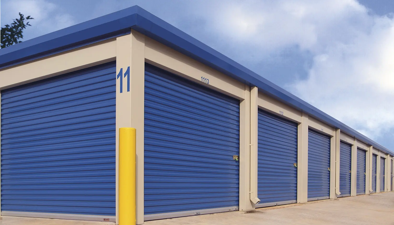 A row of blue roll-up steel doors along a self-storage building, each closing a numbered unit under a concealed hood