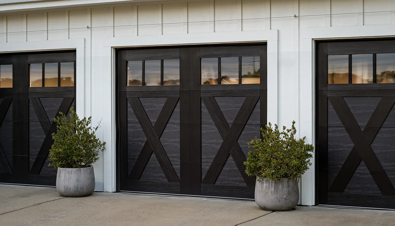 Dark wood-look carriage-house garage doors with dimensional X-bracing and square top windows