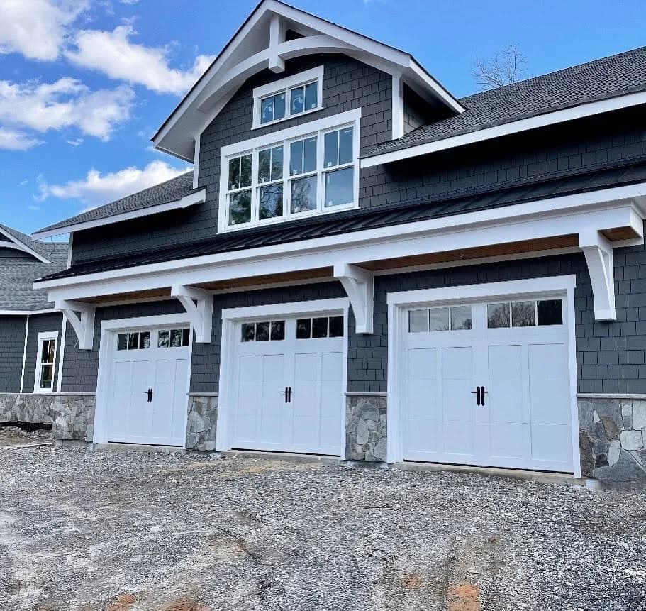 Three white raised-panel garage doors with divided-light windows on a dark craftsman-style home