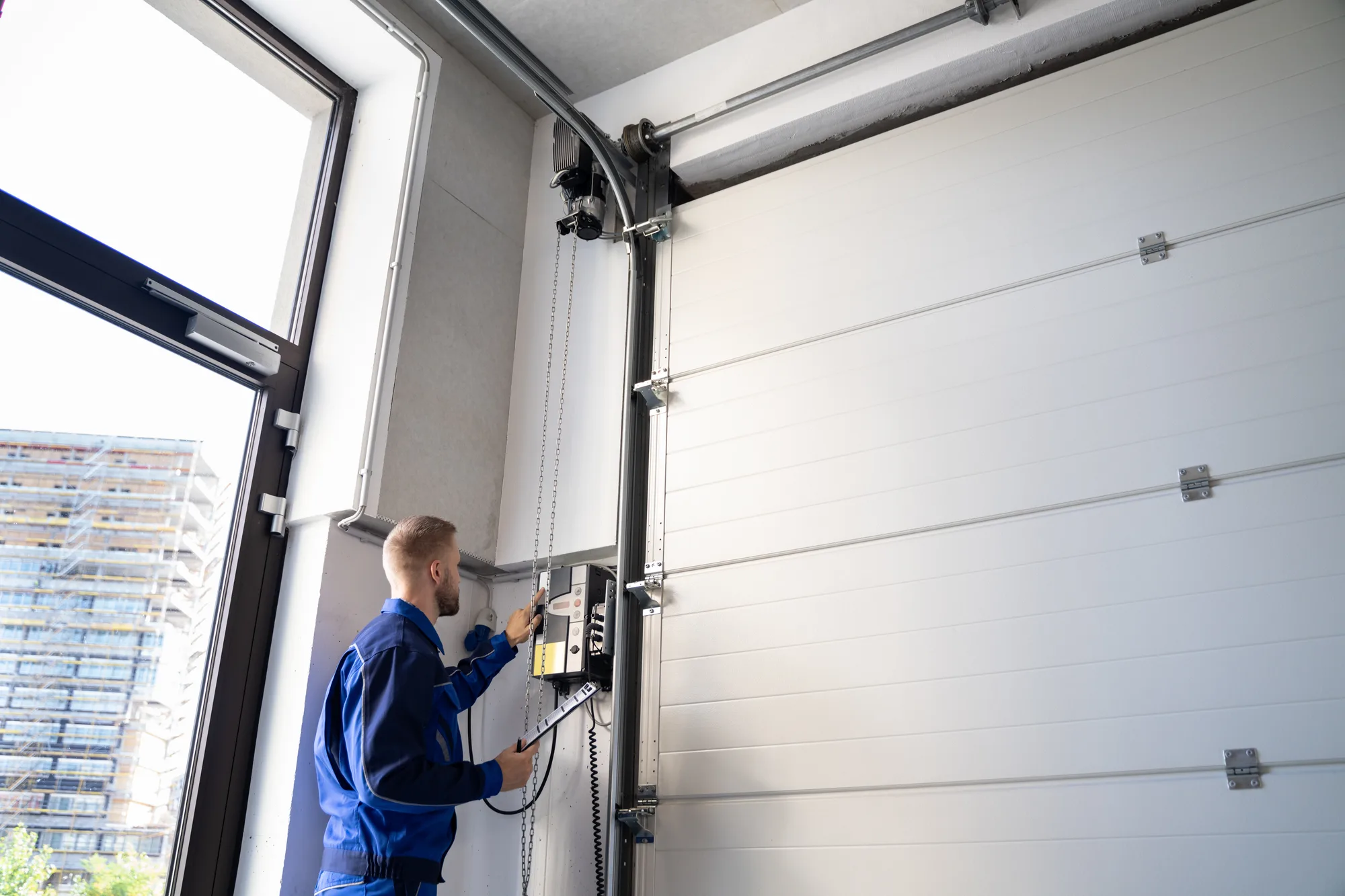 Technician adjusting a wall-mounted jackshaft garage door opener beside the vertical track of a white sectional door