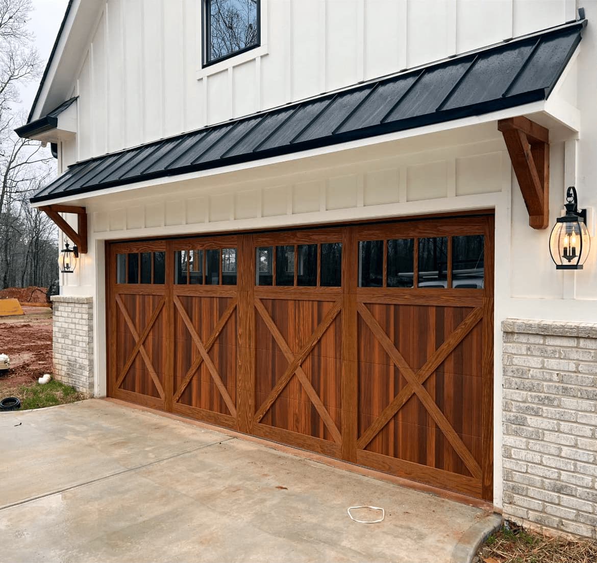 Stained wood-look carriage house garage door with X-bracing on a white board-and-batten home