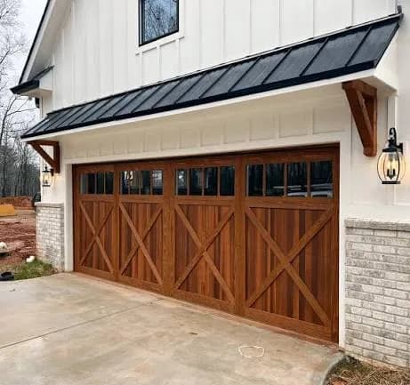 Stained wood carriage-style garage door with divided-light windows and a black metal awning