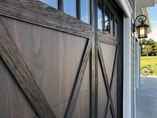 Weathered wood-look garage door with X-brace detailing and a coach-style lantern